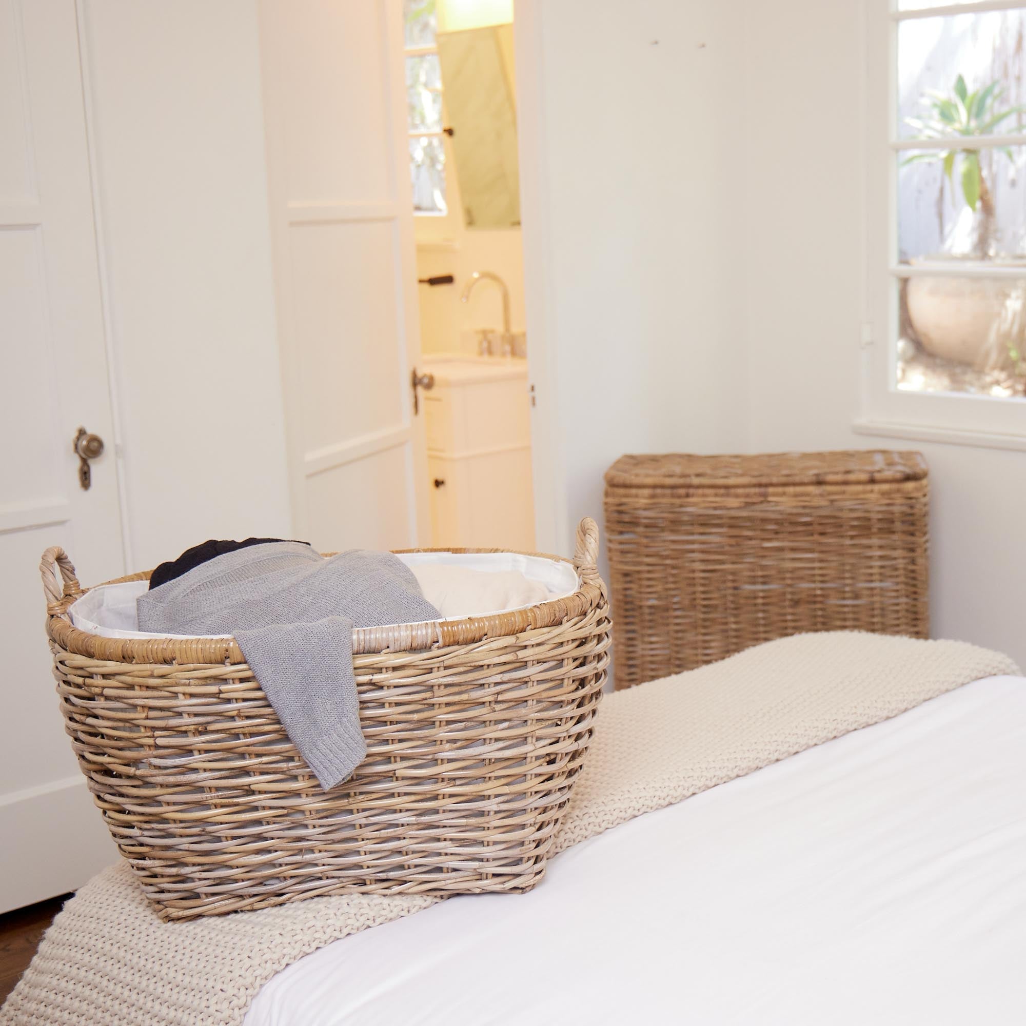 Oval Kubu Wicker Laundry Basket in Serene Grey on bed in white bedroom | The Basket Lady