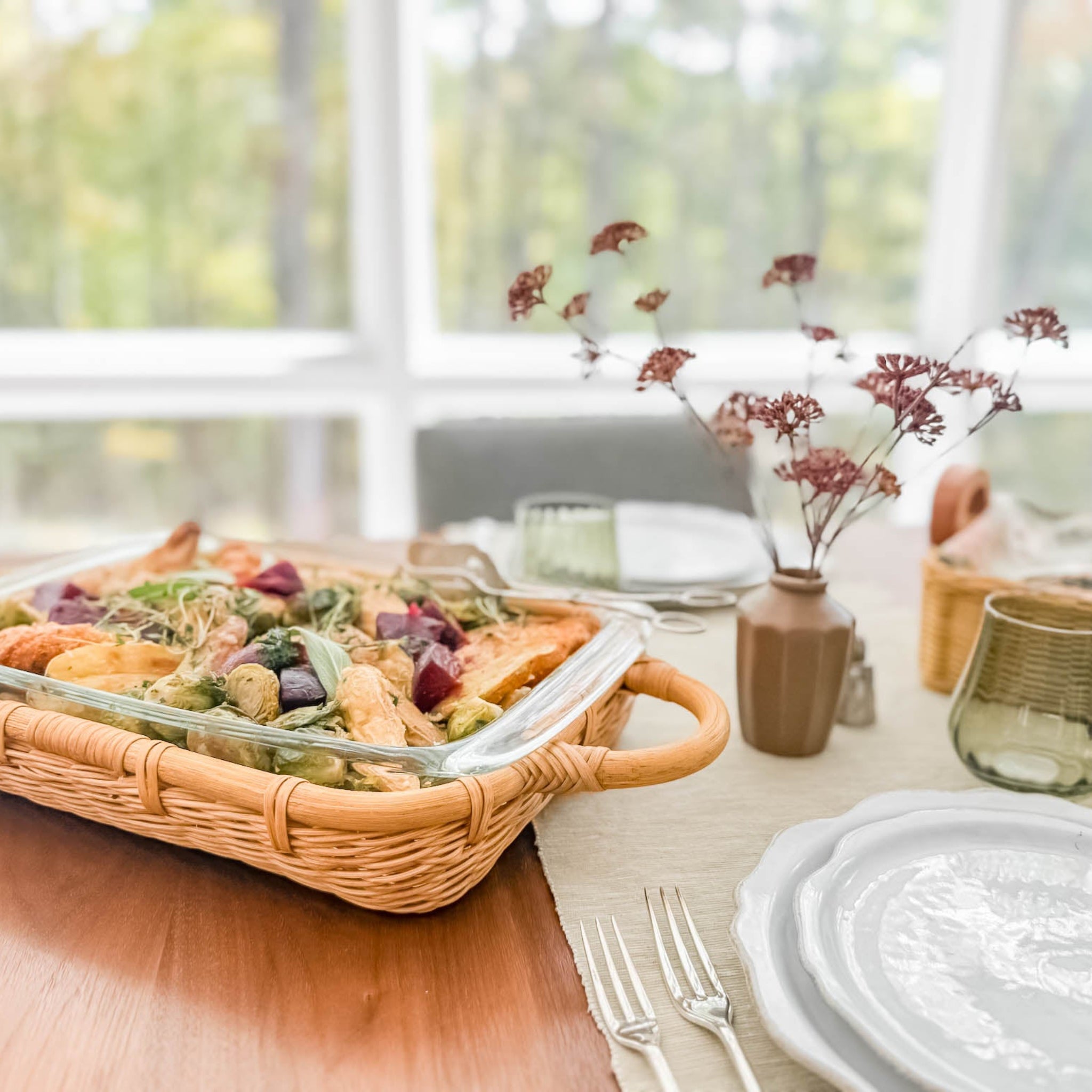 Dining table setting with a wicker casserole basket containing food, plates, and cutlery.