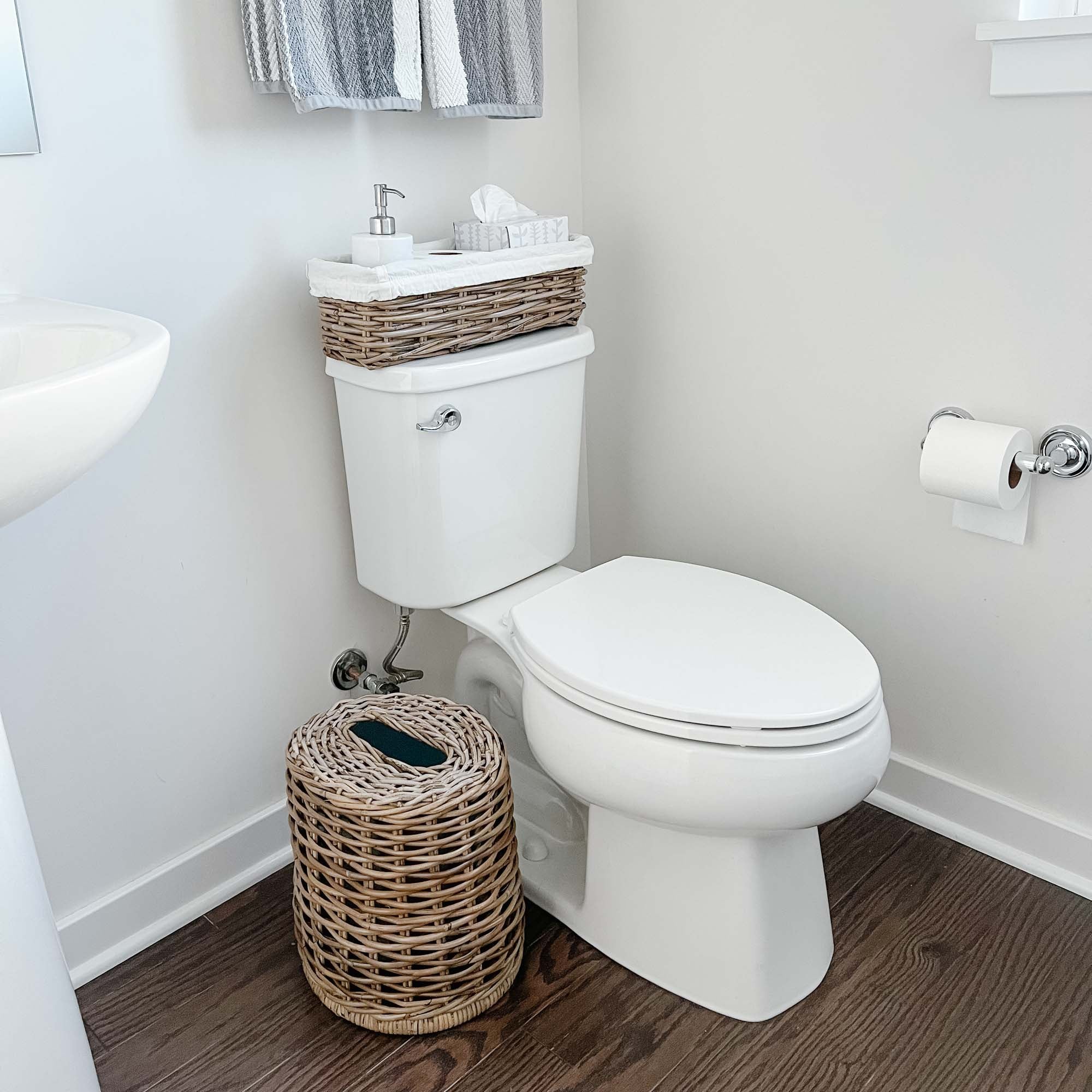 Clean white powder room with Drop-In Oval Kubu Wicker Waste Basket and Narrow Rectangular Kubu Wicker Shelf Basket size Small | The Basket Lady
